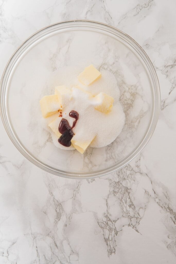 A large bowl having butter cubes, vanilla extract and sugar