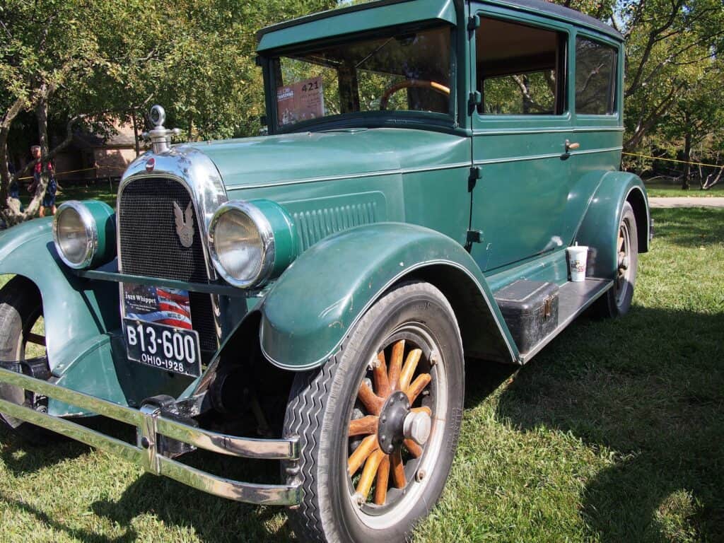 A green 1928 Whippet sedan with wooden-spoke wheels parked on grass at a car show.
