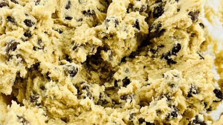 A glass bowl of homemade chocolate chip cookie dough with semisweet and milk chocolate chips folded through.