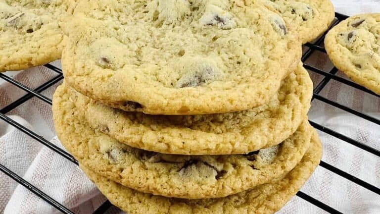 A stack of homemade chocolate chip cookies with melted semisweet and milk chocolate chips on a black cooling rack.