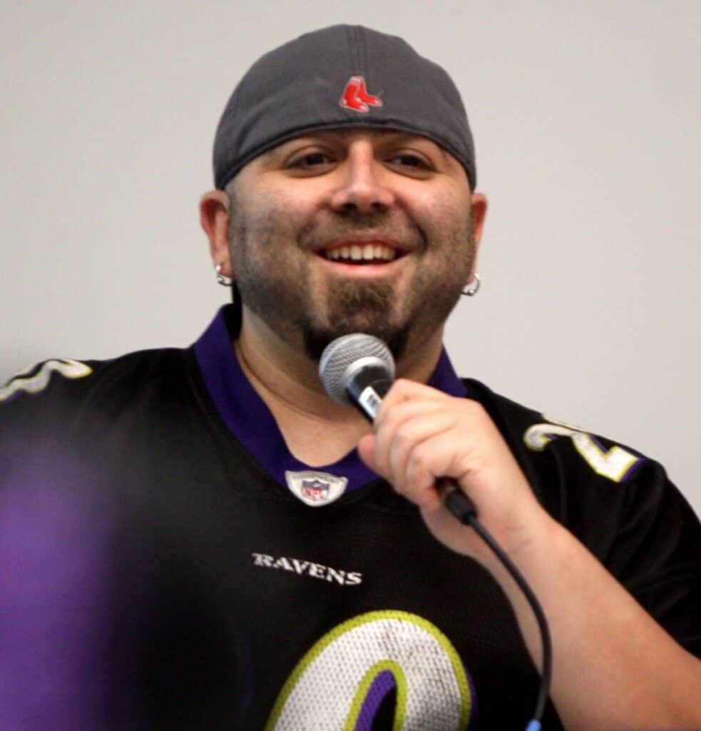 Duff Goldman, in a gray Red Sox cap and a Ravens jersey, laughs while speaking into a microphone on a panel.