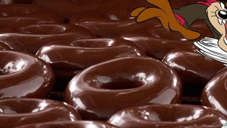 Rows of Krispy Kreme Chocolate Original Glazed doughnuts covered in shiny chocolate glaze, with the Looney Tunes character Taz at the top corner