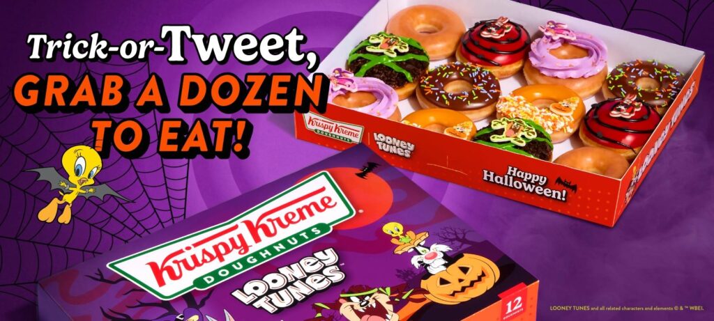 An open Krispy Kreme Looney Tunes Halloween dozen with Original Glazed doughnuts, red-iced Bugs Bunny doughnuts, purple-swirled Lola Bunny doughnuts, chocolate-and-green Taz doughnuts, orange candy corn Tweety and Sylvester doughnuts and chocolate doughnuts with sprinkles, beside a closed purple Looney Tunes box with Tweety, Sylvester and Taz on the lid.