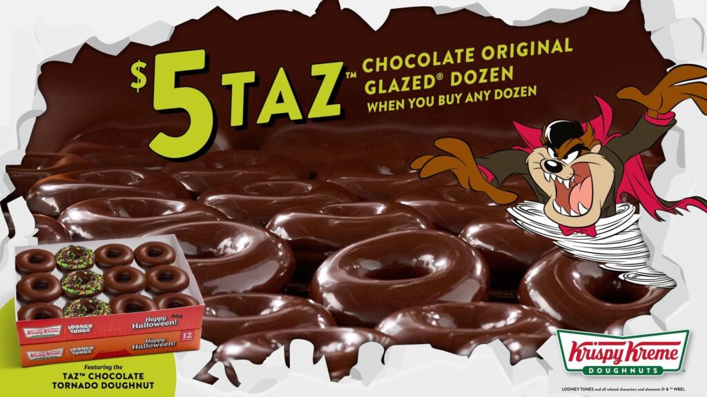 Krispy Kreme's promotional image for its $5 Taz Chocolate Original Glazed Dozen: a Looney Tunes Halloween box holding nine chocolate-glazed doughnuts and three topped with green icing and sprinkles, in front of rows of chocolate-glazed doughnuts and a cartoon Taz in a vampire cape.